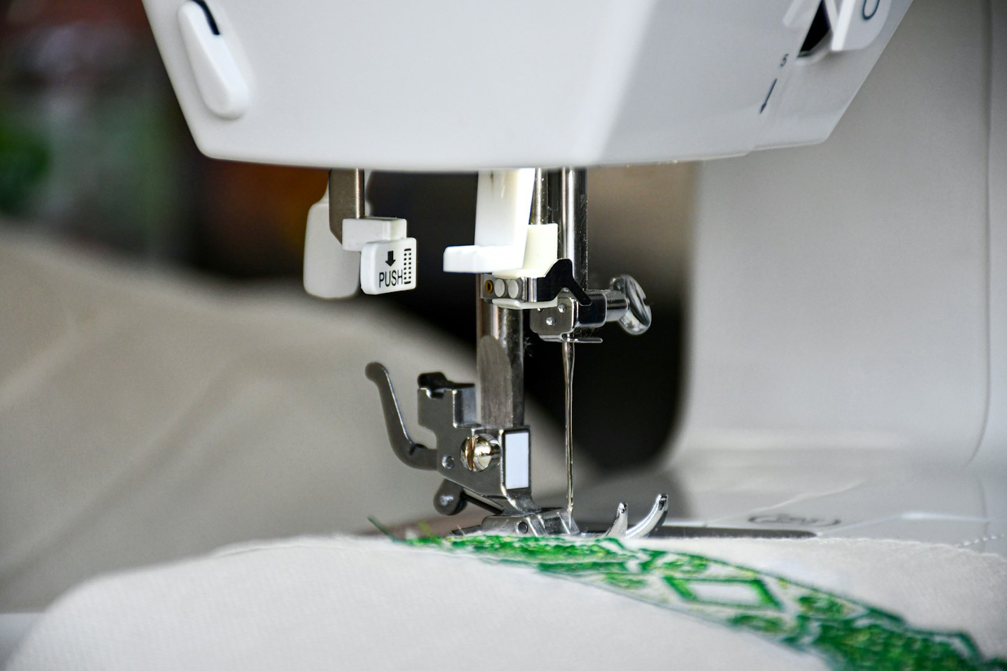 A sewing machine needle stitching patterns into white fabric.