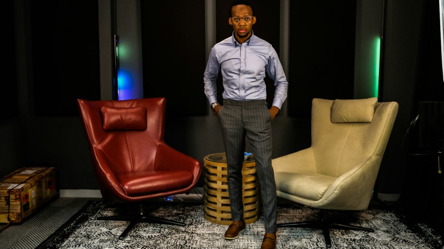 Man in a blue shirt standing between two armchairs.