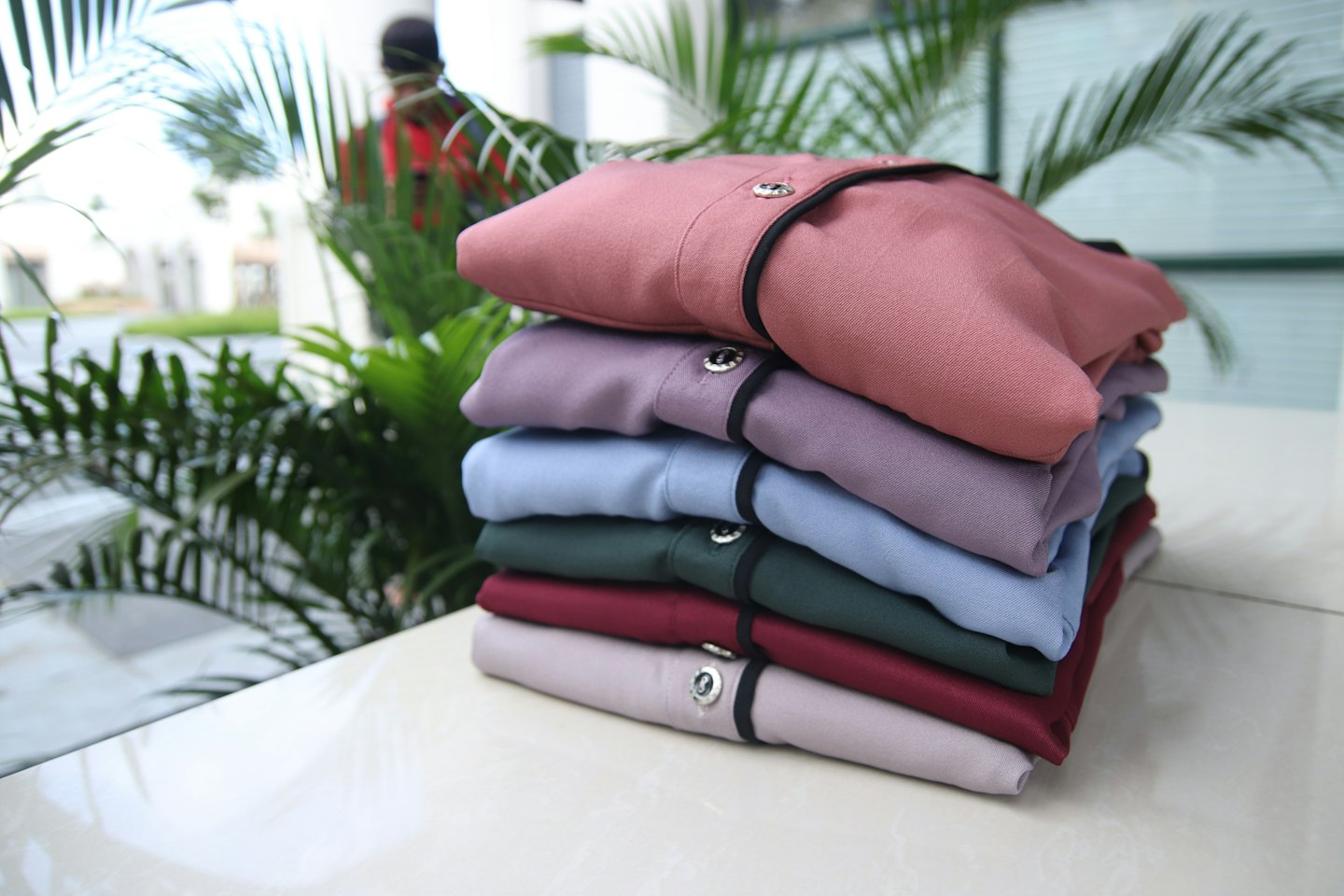A stack of six folded long-sleeved shirts rests on a white surface.