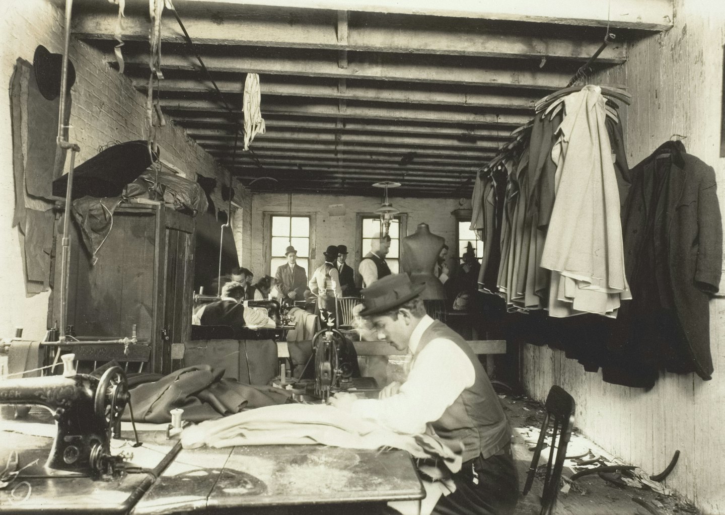 Tailors work on vintage sewing machines in a busy workshop.