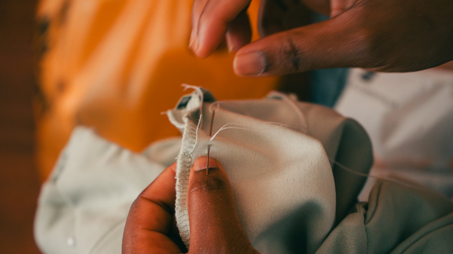 Hands carefully hand-stitch light fabric with a needle and thread.