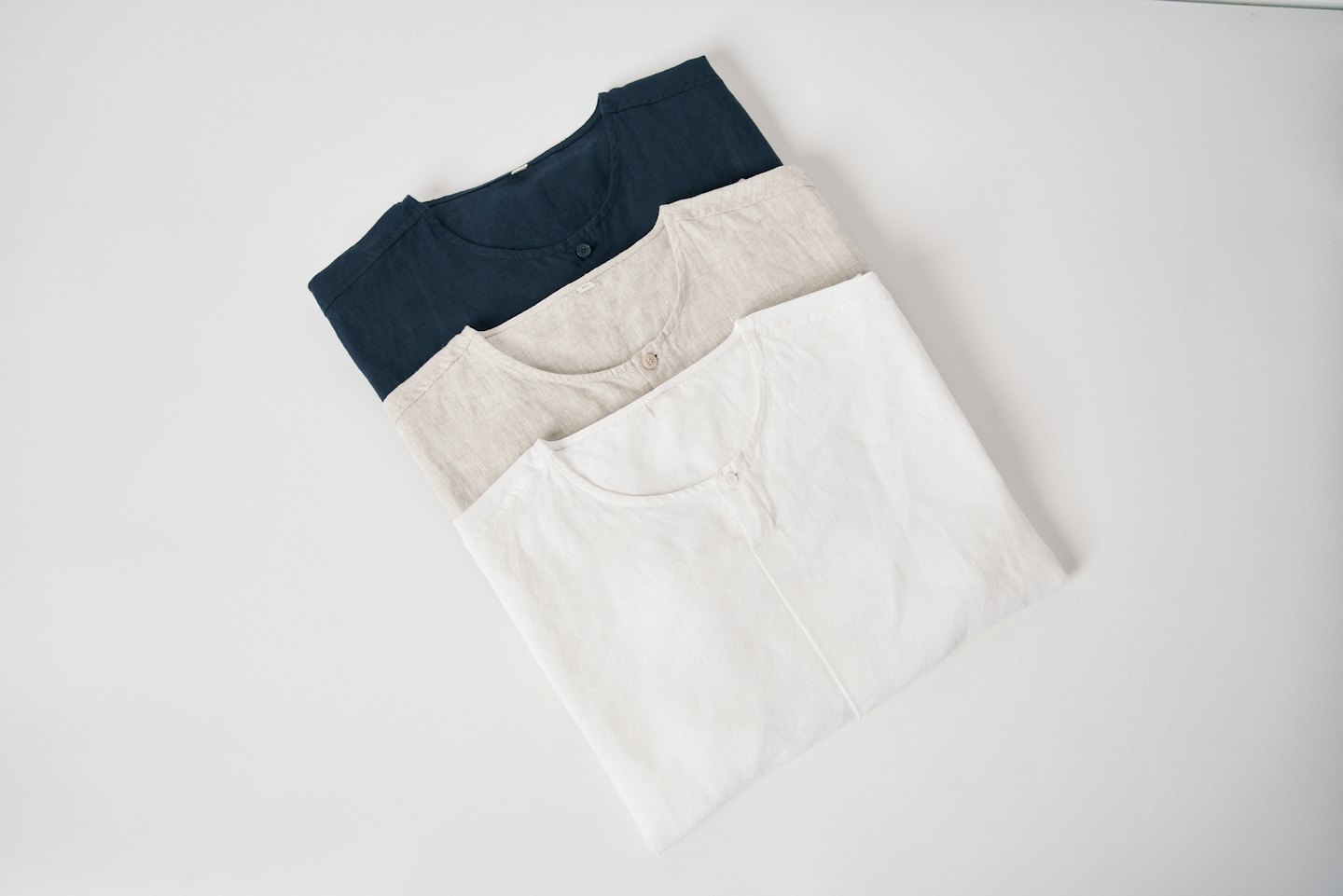 Three folded linen shirts stacked neatly on a flat surface.