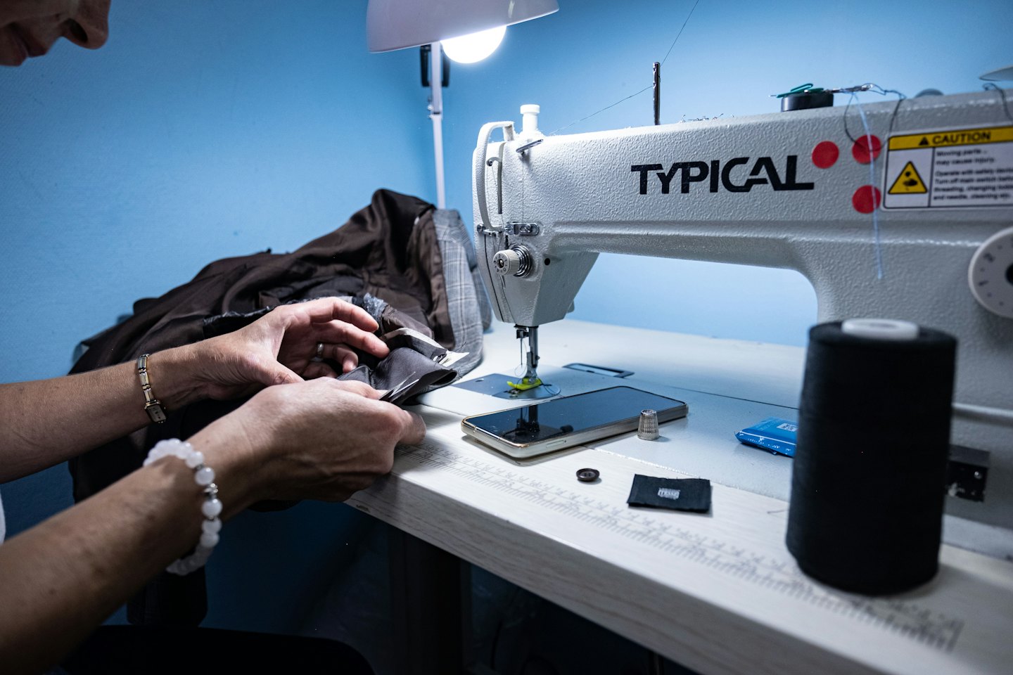 Hands sewing brown fabric on an industrial machine.